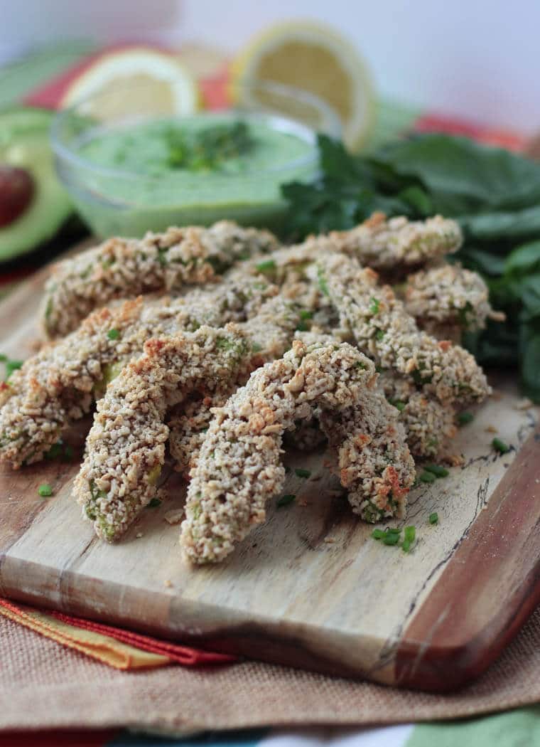 A stack of baked avocado fries with dip in the background.