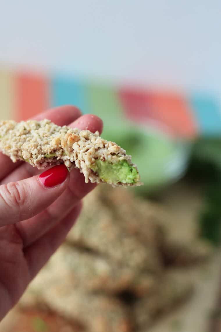 A hand holding a bitten avocado fries.