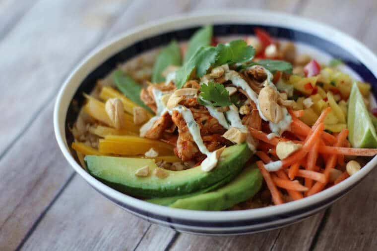 close up of paleo cauliflower rice chicken burrito bowl garnished with herbs and nuts in a black and white bowl 