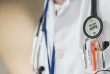 Close up of a doctor's labcoat with pens in the pocket and a stethescope around their neck.