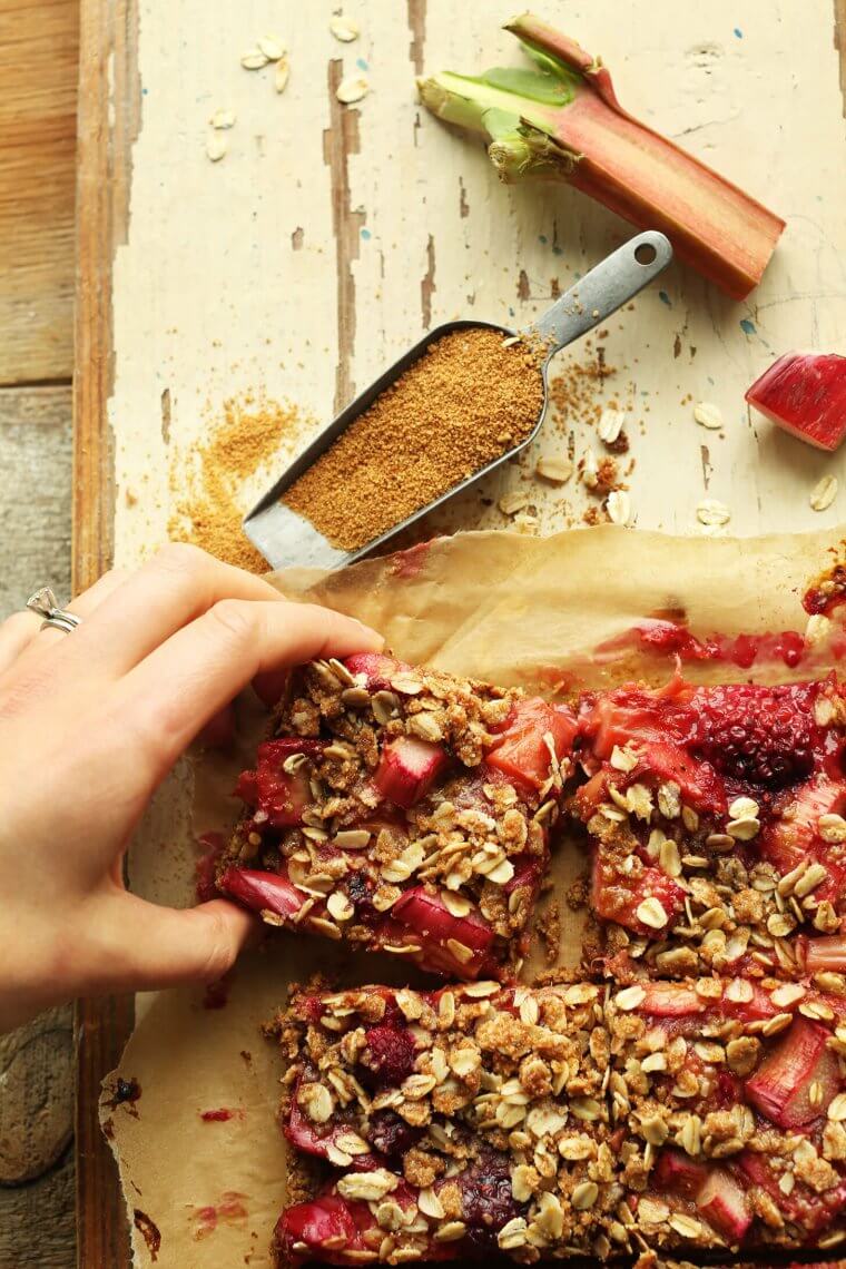 A hand grabbing a bar of strawberry rhubarb crumble bars.