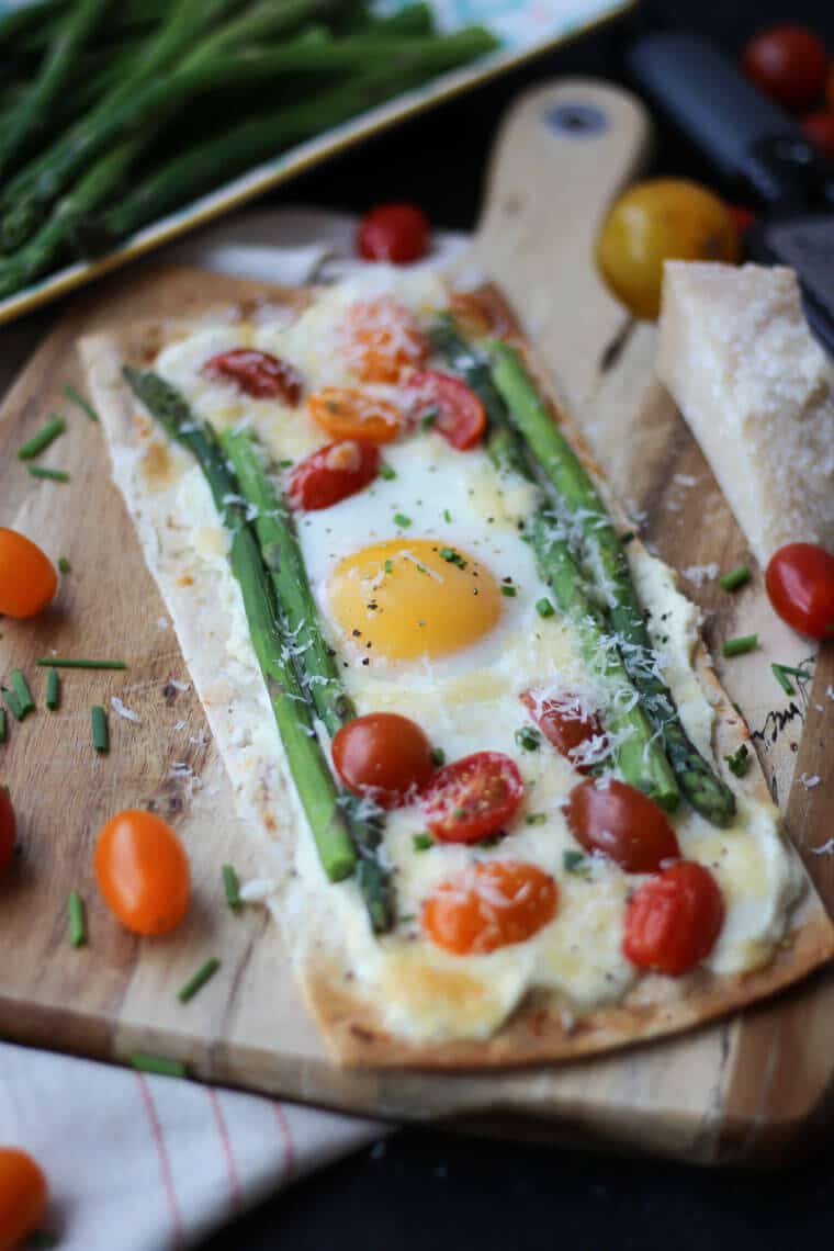 A breakfast pizza with egg, tomatoes, and asparagus.  