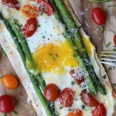 A breakfast pizza with egg, tomatoes, and asparagus with a fork beside it.