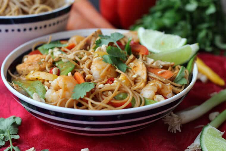 A bowl with lychee chicken curry noodles with cilantro on top and limes.