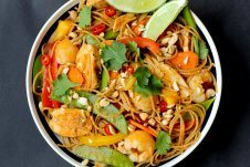 An overhead image of a bowl of healthy lychee chicken curry noodles with garnish and limes on top.