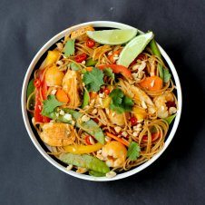 An overhead image of a bowl of healthy lychee chicken curry noodles with garnish and limes on top.