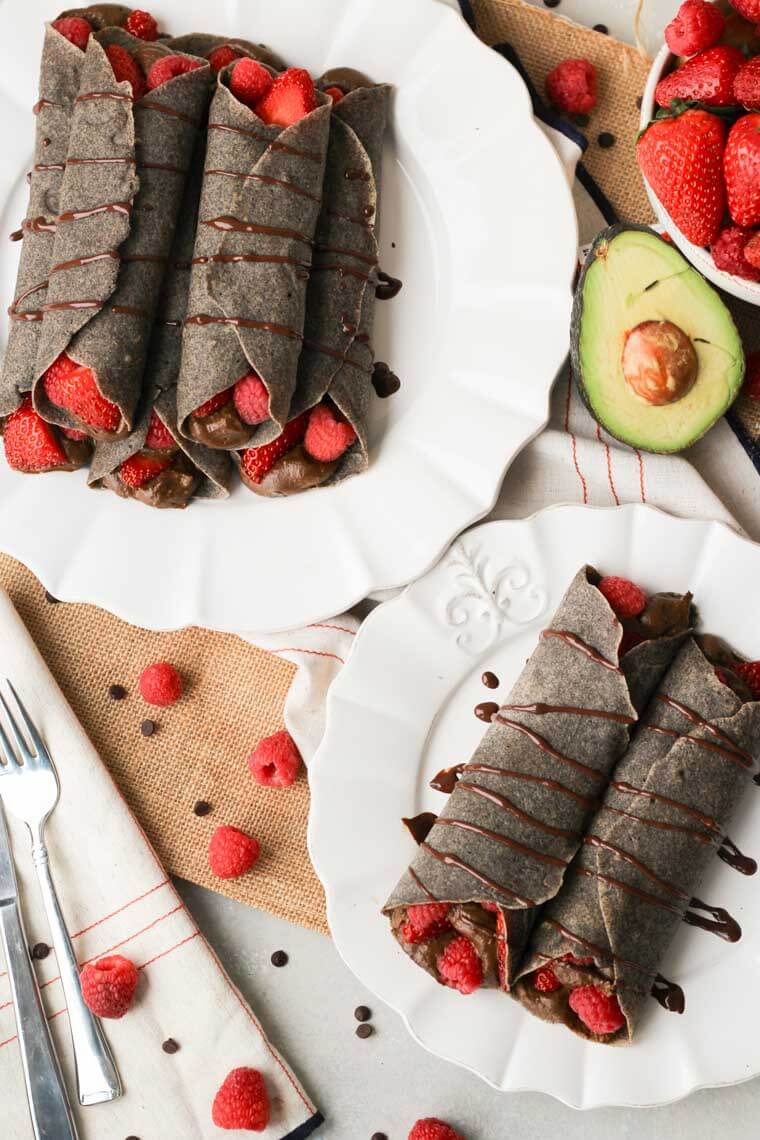 An overhead photo of two white plates with multiple crepes made with buckwheat and chocolate on each.