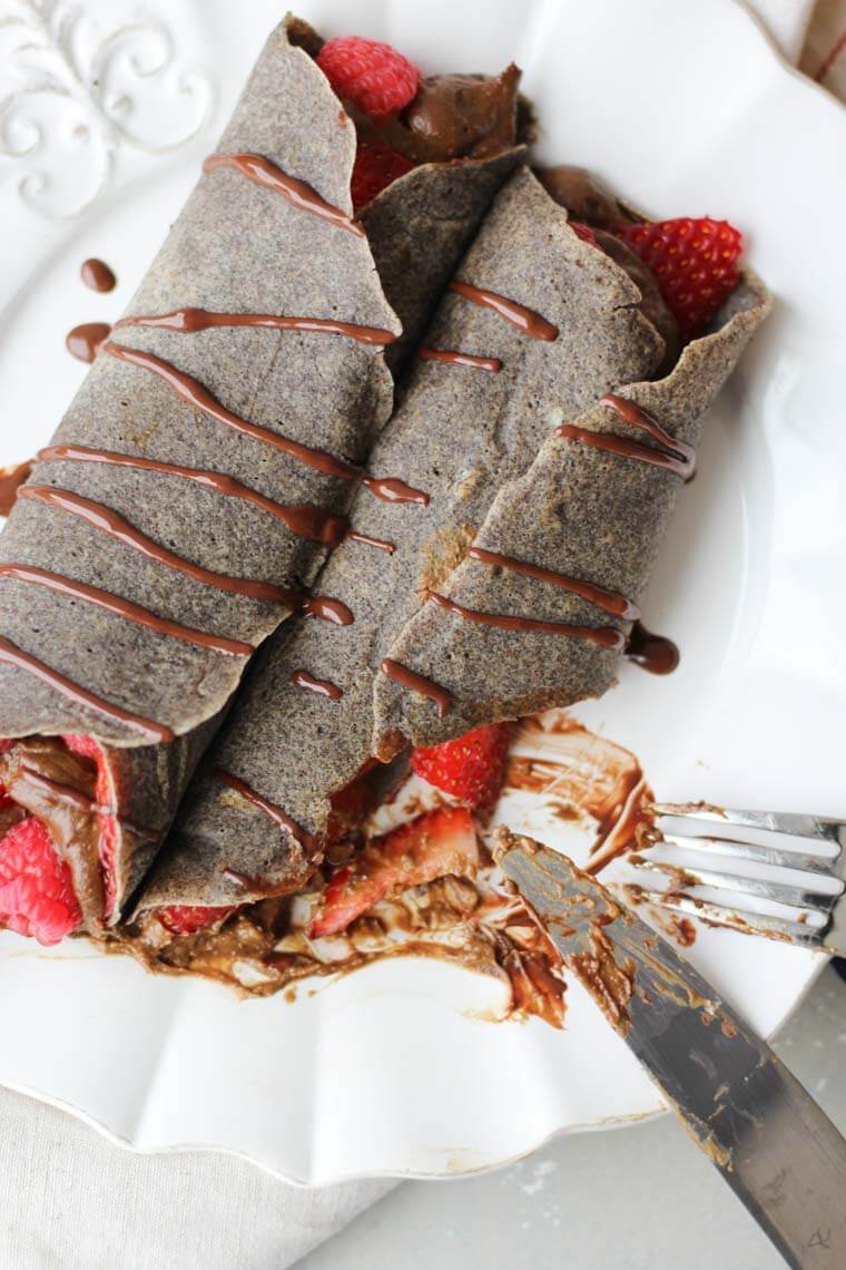 A chocolate buckwheat crepe being cut with a knife and fork.