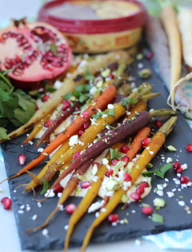 Honey roasted carrots on top of a bed of creamy hummus sauce topped with pomegranate.