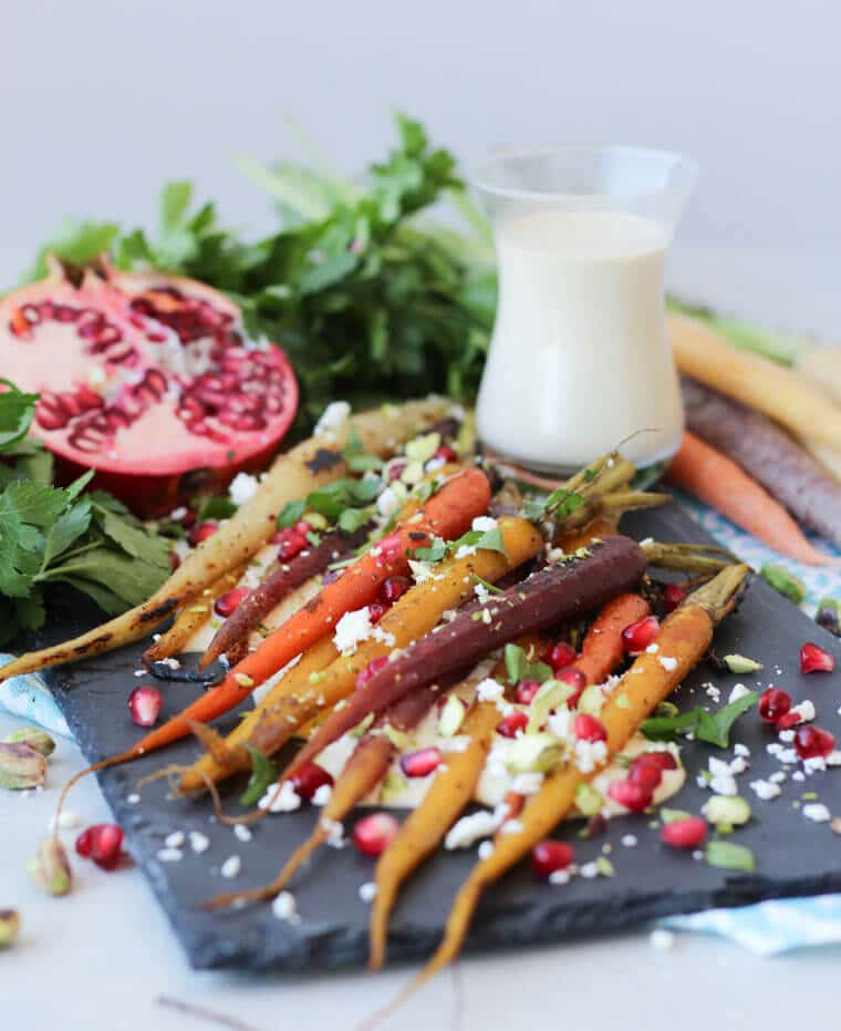 Za’atar Honey Roasted Carrots on a black serving plate topped with pomegranate and parsley.