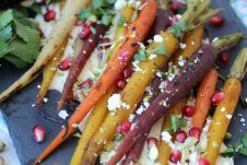 A close up of roasted carrots with pomegranate seeds and cheese sprinkled on top.