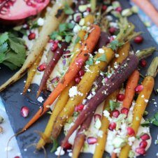 A close up of roasted carrots with pomegranate seeds and cheese sprinkled on top.