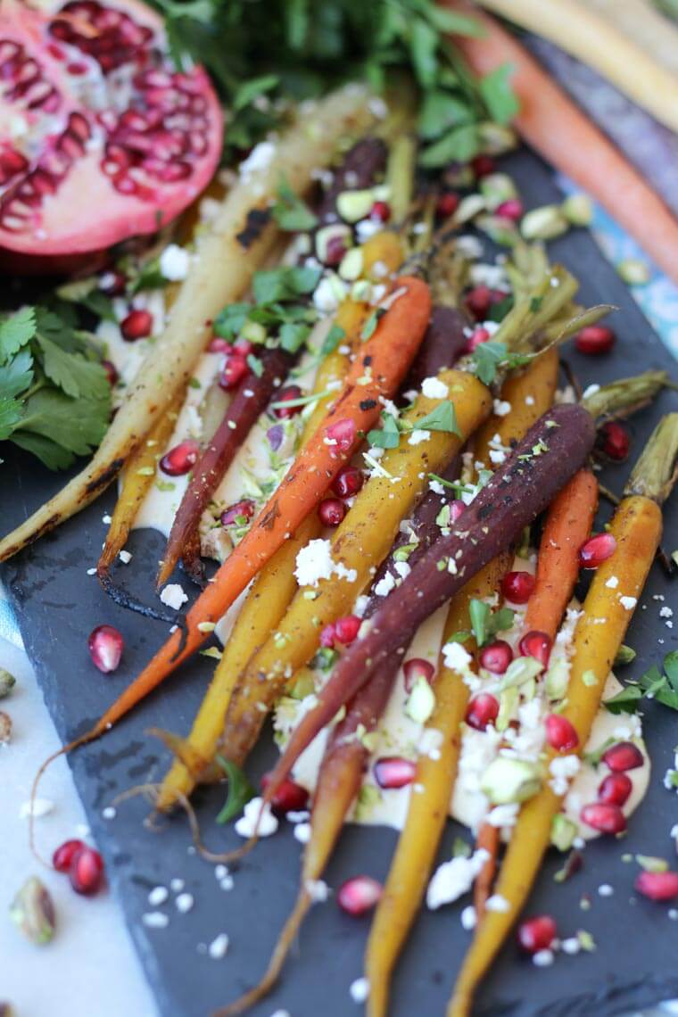 A close up of roasted carrots with pomegranate seeds and cheese sprinkled on top.