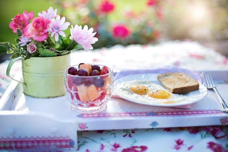 A photo of a glass filled with fruit on a table with a plate of eggs beside it.