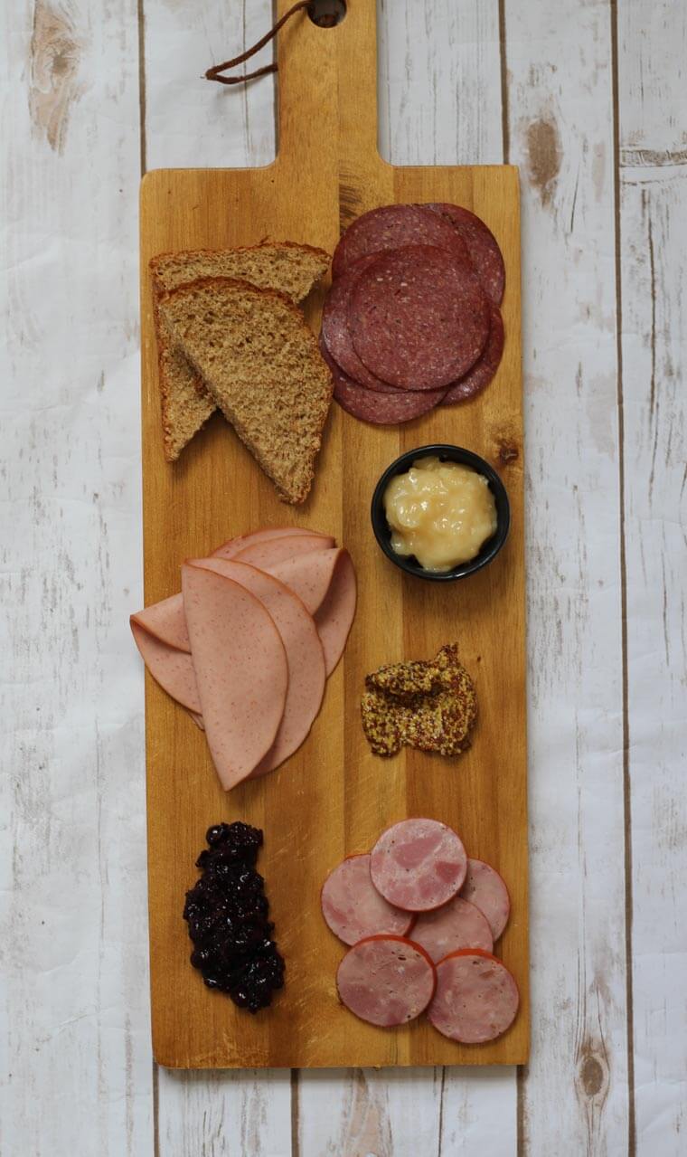 A wooden serving platter with charcuterie on it, such as cheese, sliced meats, bread slices, and nuts.