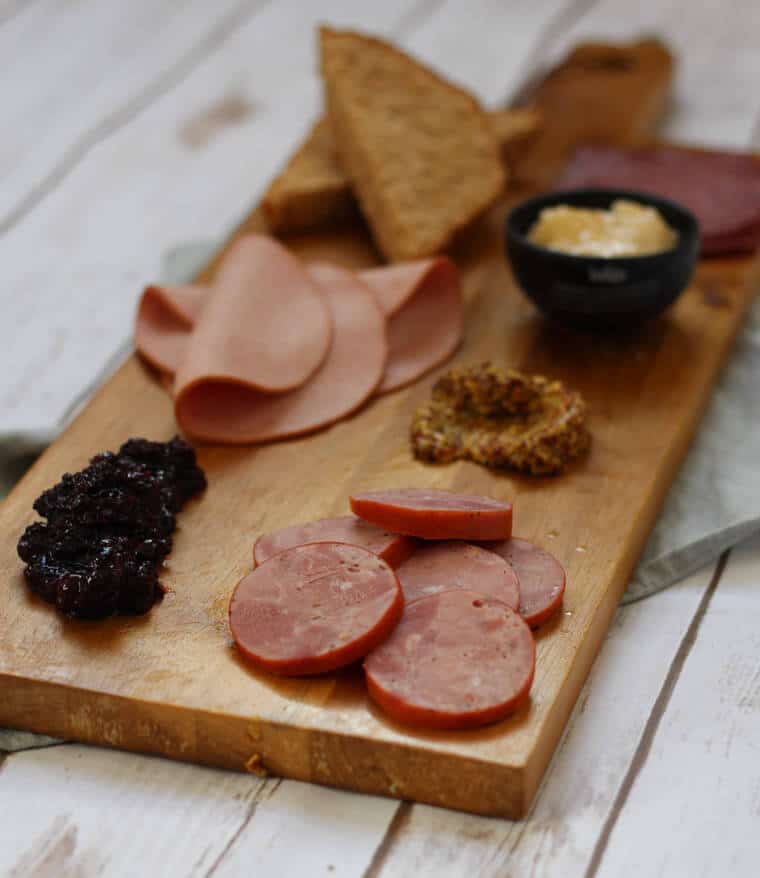 An angled image of a wooden serving platter with charcuterie on it, such as cheese, sliced meats, bread slices, and nuts.