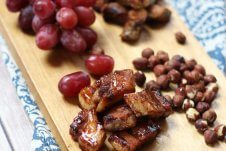 A serving platter with charcuterie on it, such as grapes, meats, and nuts.