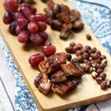 A serving platter with charcuterie on it, such as grapes, meats, and nuts.