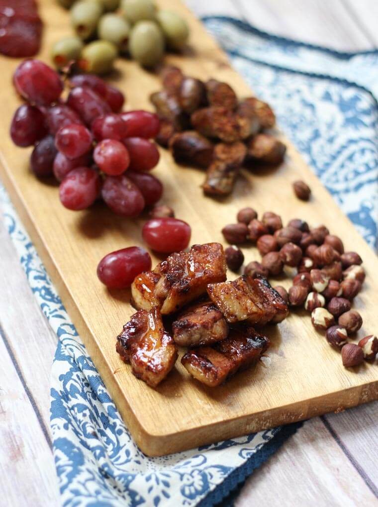 A serving platter with charcuterie on it, such as grapes, meats, and nuts.