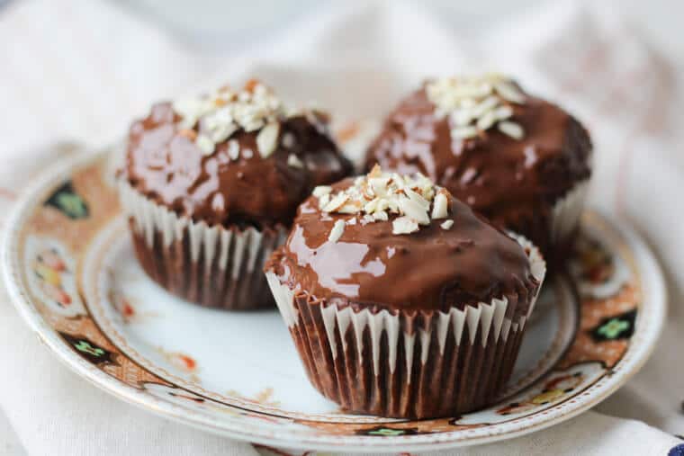 A plate of three chocolate cherry almond muffins with a chocolate glaze with almonds on top.