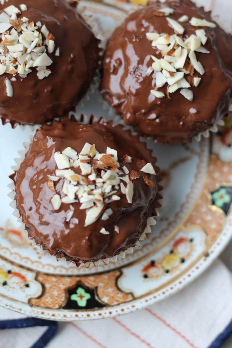 An overhead close up photo of chocolate cherry almond muffins with a chocolate glaze with almonds on top.