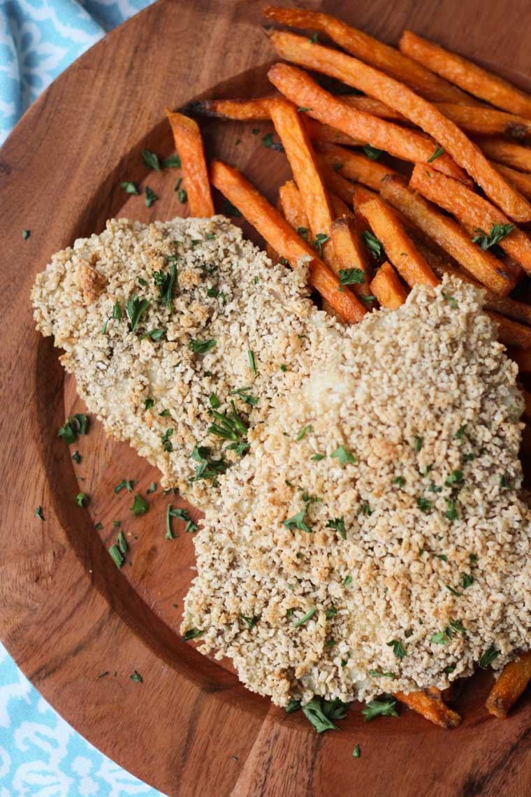 A close up photo of a brown plate with two gluten free fish and sweet potato chips.