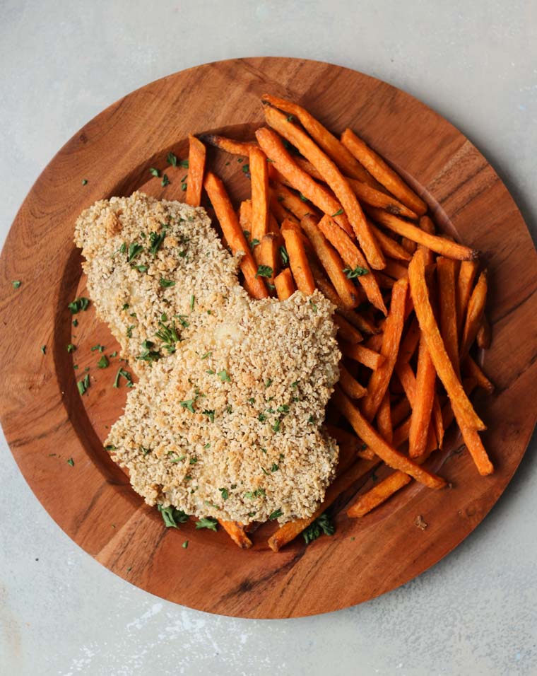 An overhead photo of a brown plate with two gluten free fish and sweet potato chips.