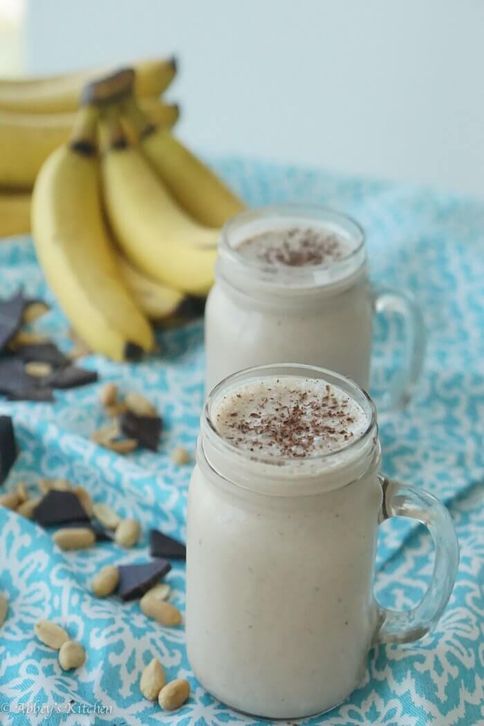 Two glasses of peanut butter banana smoothies with bananas in the background.