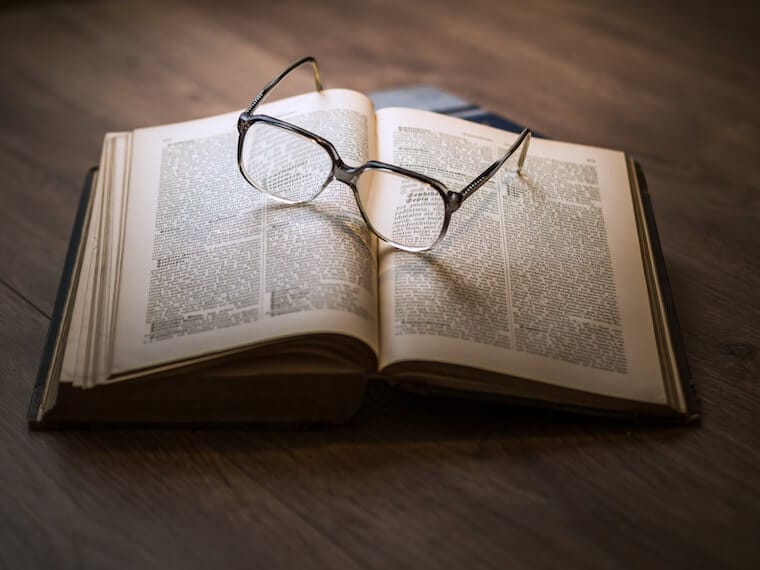 An opened book with a pair of glasses on top.