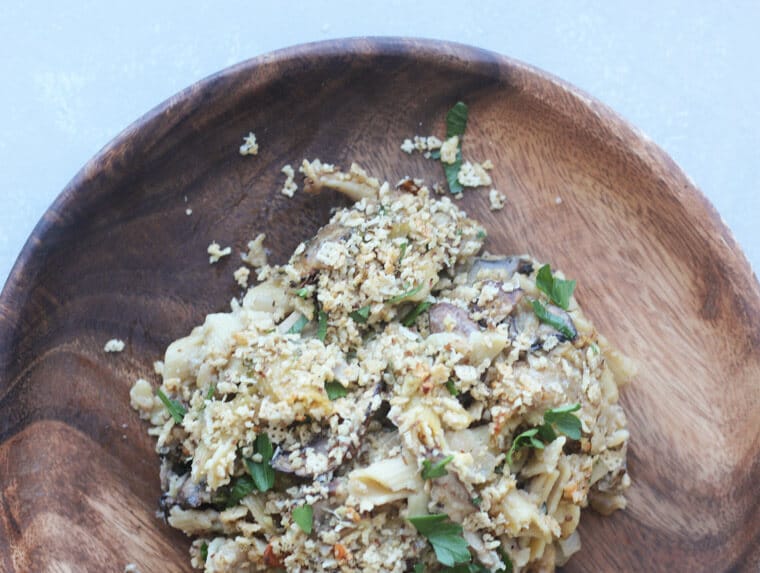 A serving of mushroom penne pasta bake on a wooden plate.