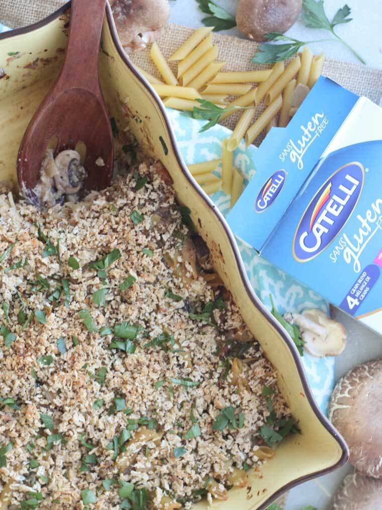 A baking dish with a wooden spoon scooping the mushroom penne pasta bake.