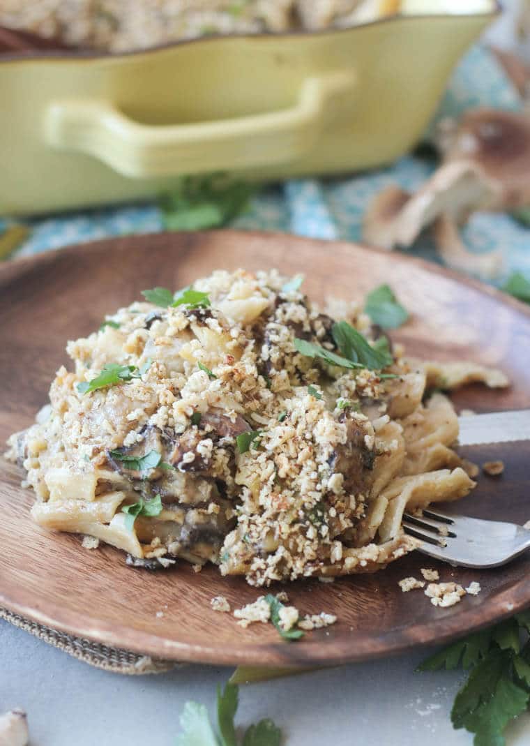 A serving of mushroom penne pasta bake on a wooden plate with a fork in it.