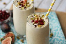 Two glasses of pistachio smoothies with fig toppings and paper straws.