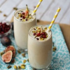 Two glasses of pistachio smoothies with fig toppings and paper straws.