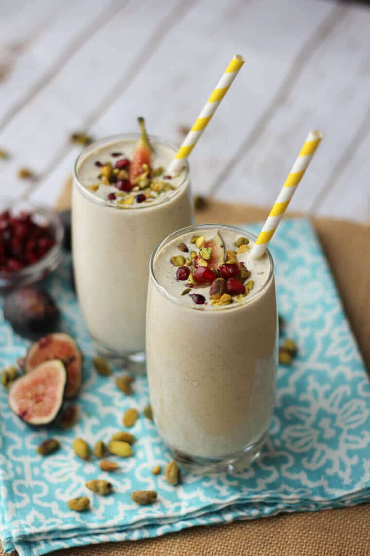 Two glasses of pistachio smoothies with fig toppings and paper straws.