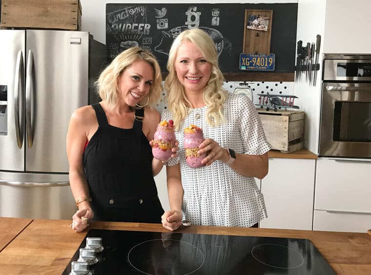 Abbey Sharp standing in a kitchen with another woman holding two mason jars of overnight oats.