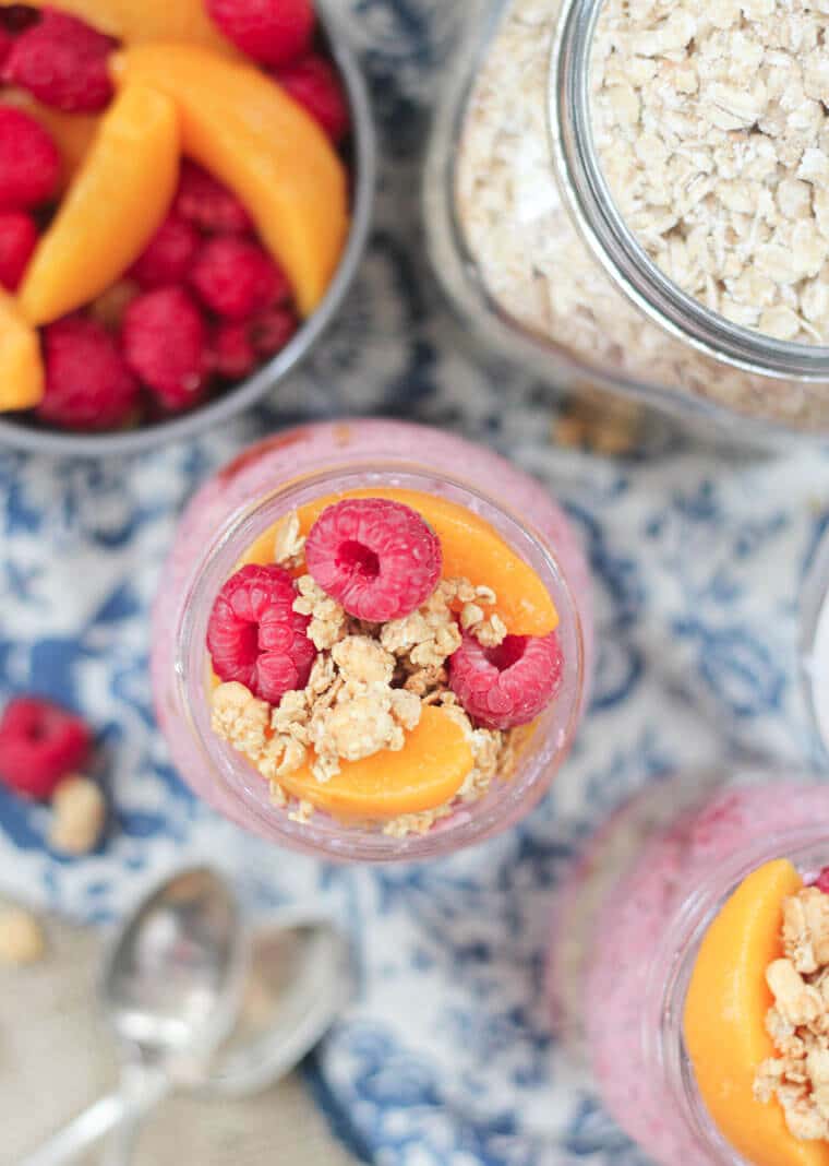 An overhead photo of a jar of overnight oats topped with raspberries and peaches.