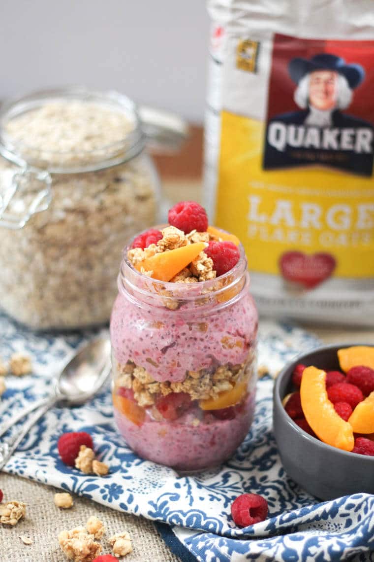 A mason jars containing peach melba crumble overnight oats topped with peaches and raspberries.