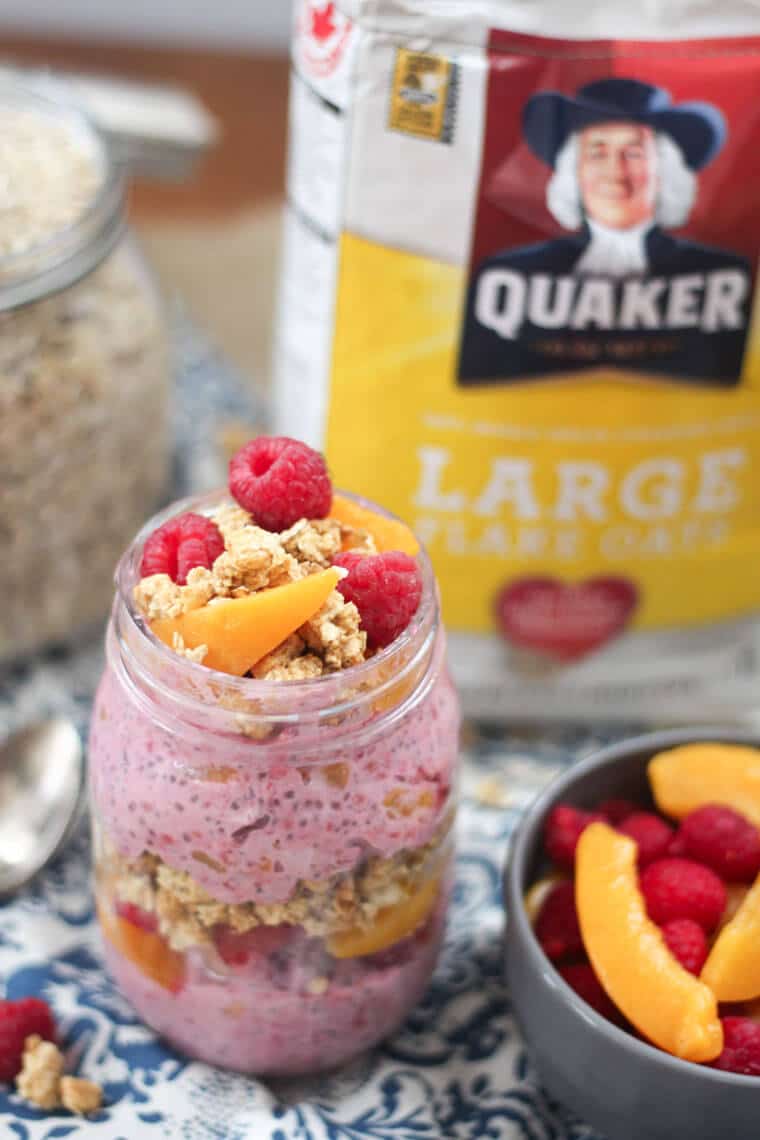 A mason jars containing peach melba crumble overnight oats with a bag of Quaker large flake oats in the background.