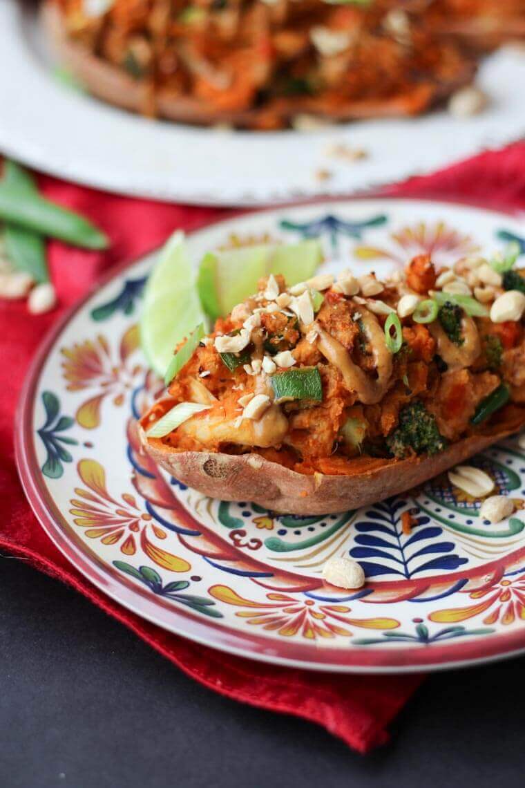 close up of paleo peanut satay sweet potato on a colourful dish garnished with nuts and fresh lime