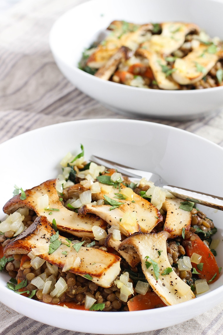 Cooked lentils in two white bowls topped with oyster mushrooms.