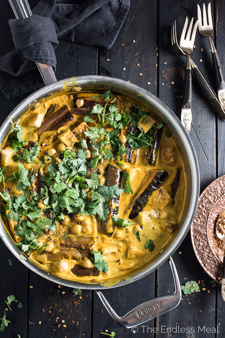 Tofu and eggplant curry in a saucepan, topped with parsley on a black surface.