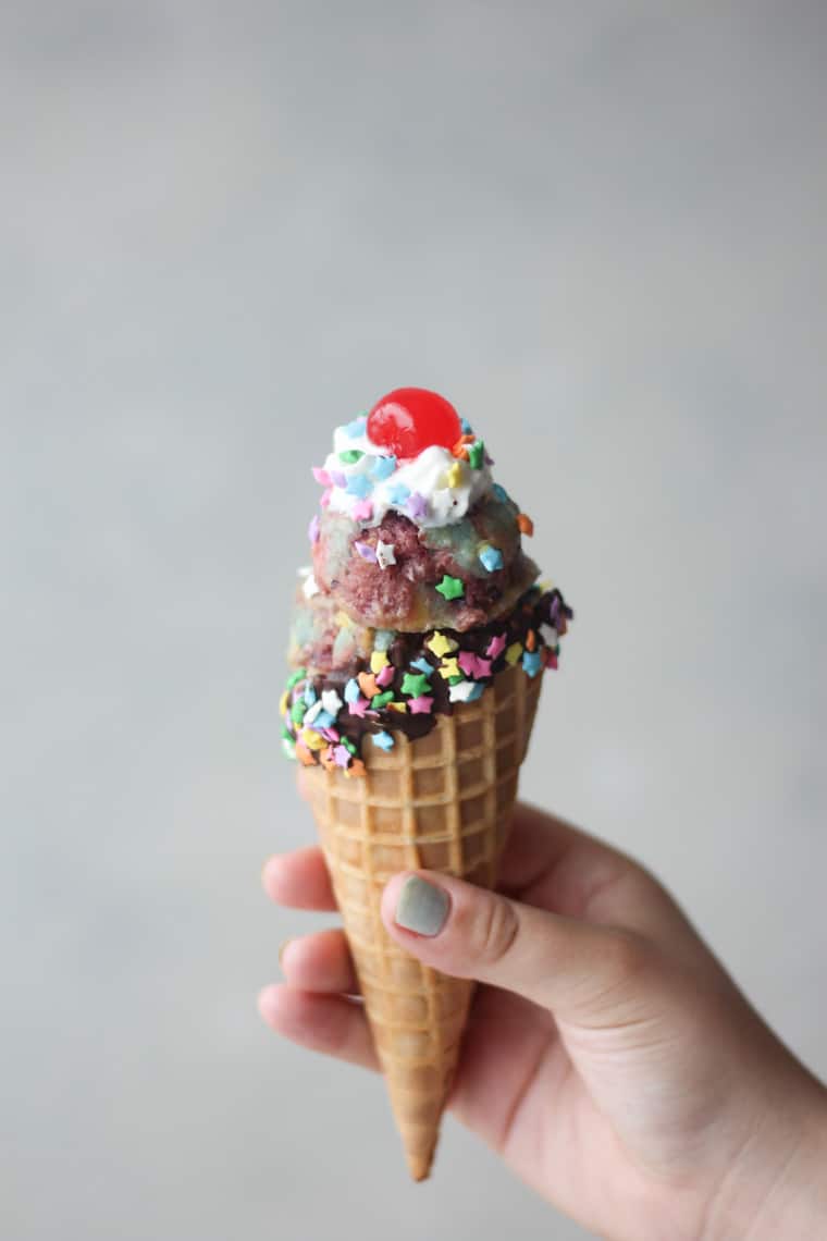 Unicorn nice cream in a chocolate coated cone with sprinkles and cherry.