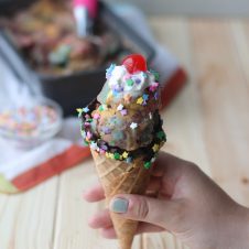 A hand holding a cone with ice cream in it with a dollop of whipped cream on top and a cherry.