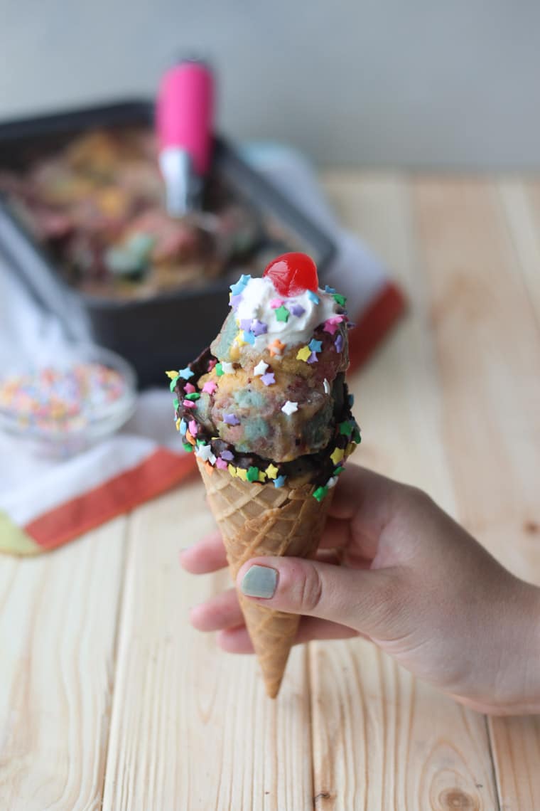 A hand holding a cone with ice cream in it with a dollop of whipped cream on top and a cherry.