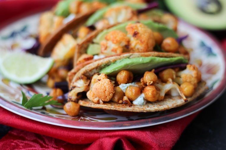 Close up of vegan cauliflower and chickpea tacos with avocado and cilantro on a colourful plate.