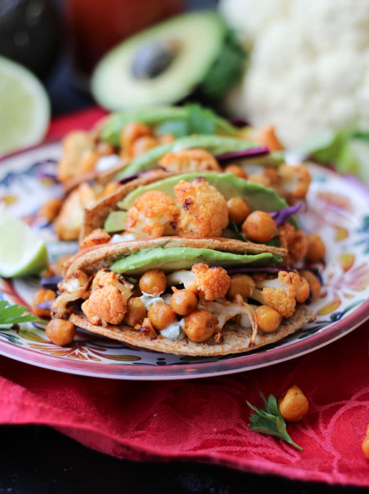 Close up of buffalo cauliflower and chickpea tacos on a colourful plate with lime on the side.