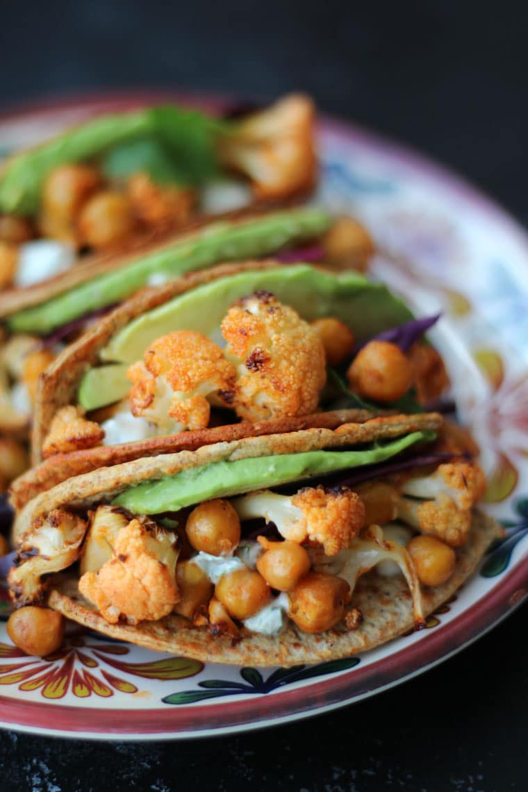 Close up of vegan buffalo cauliflower taco recipe topped with avocado on a colourful plate.