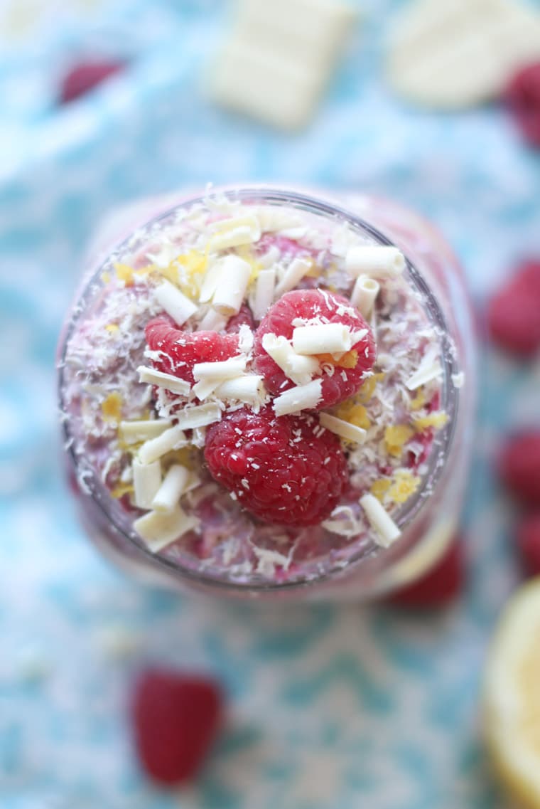A close up of an overhead view of mason jar containing white chocolate, lemon, raspberry overnight oats.