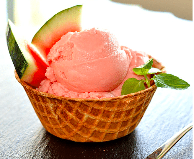 Pink nice cream in a cone garnished with watermelon slices. 